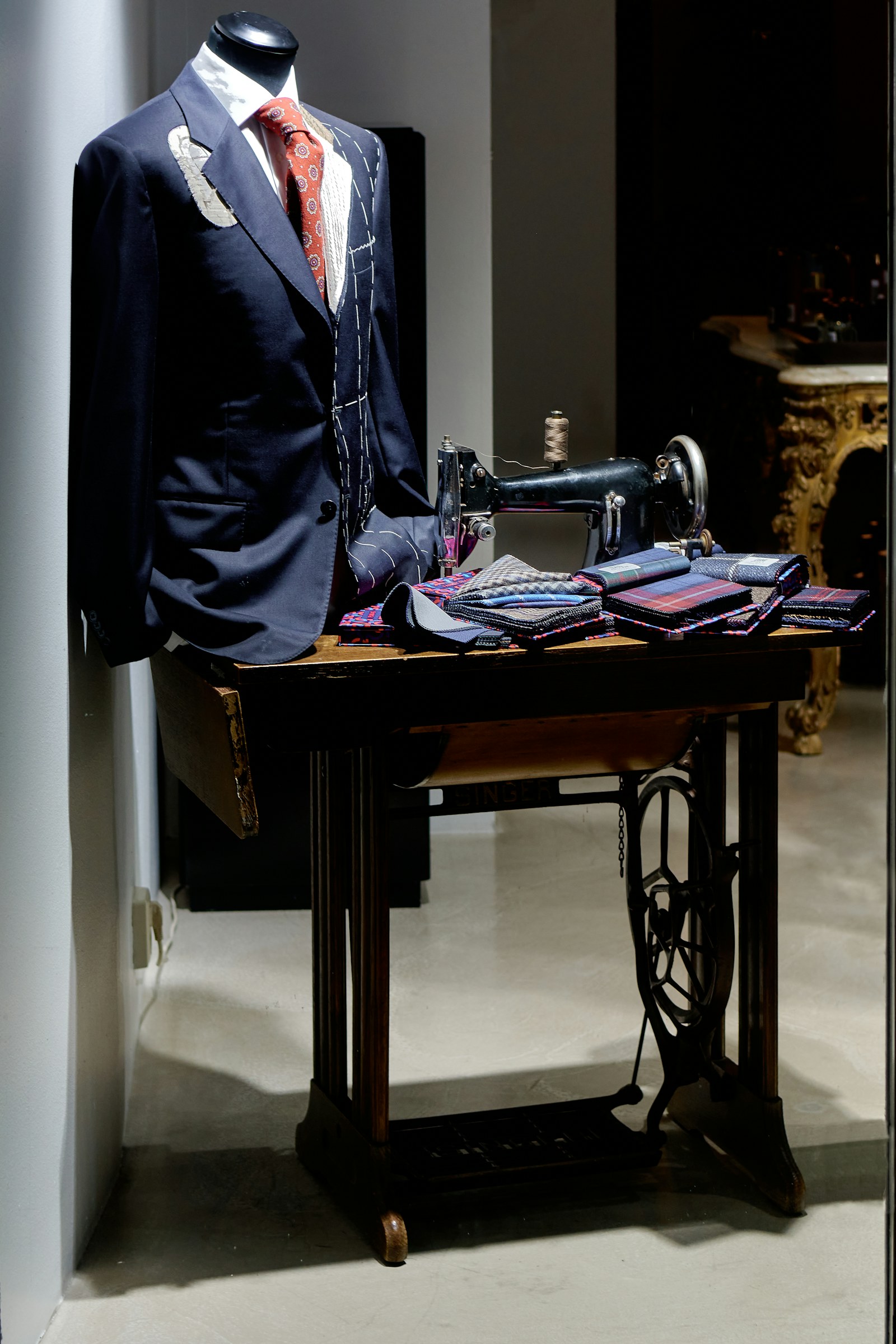 Navy jacket in white basting thread on a tailor's form beside a vintage Singer machine