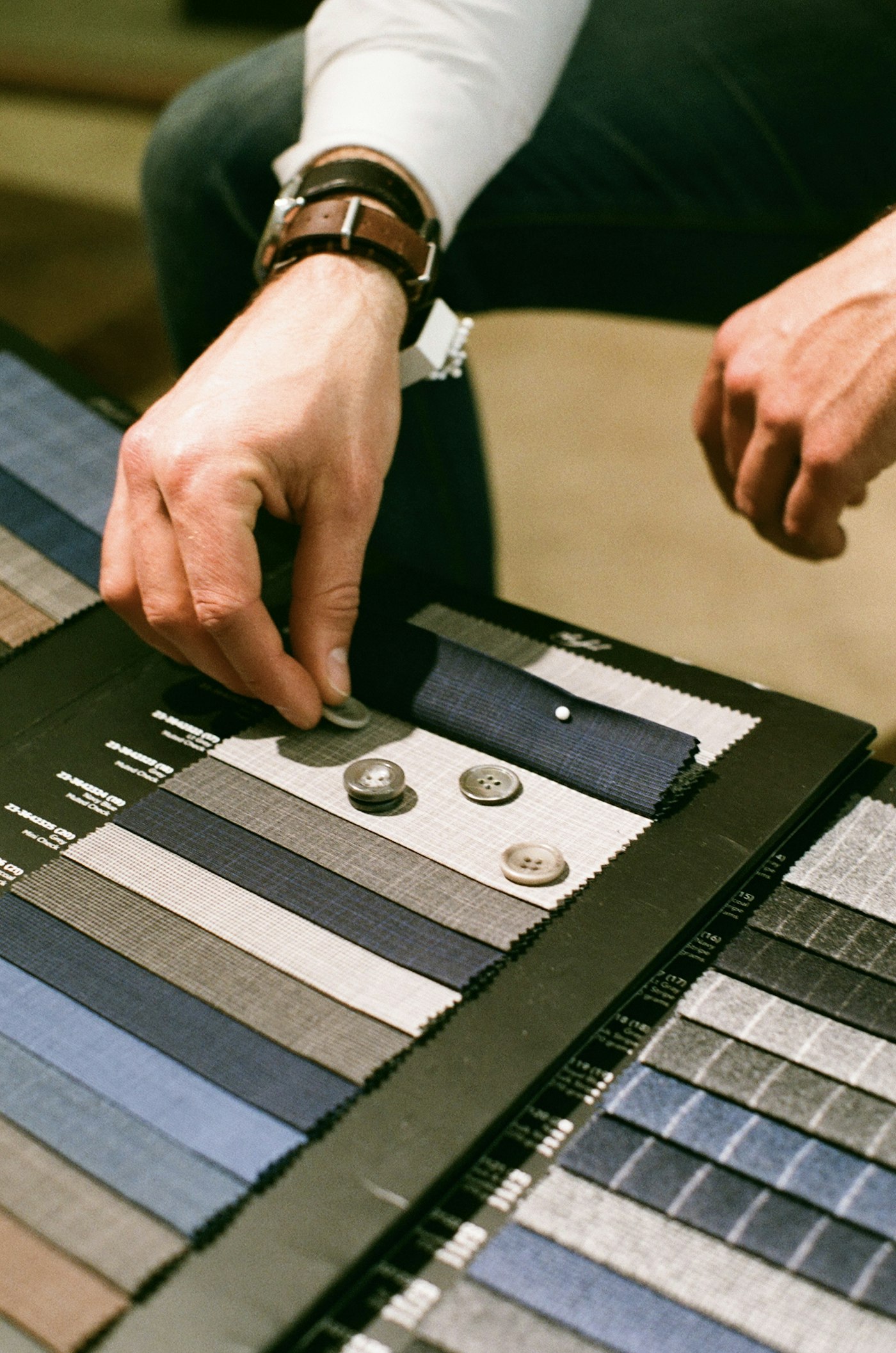 Hands selecting suiting swatches and horn buttons from a fabric book
